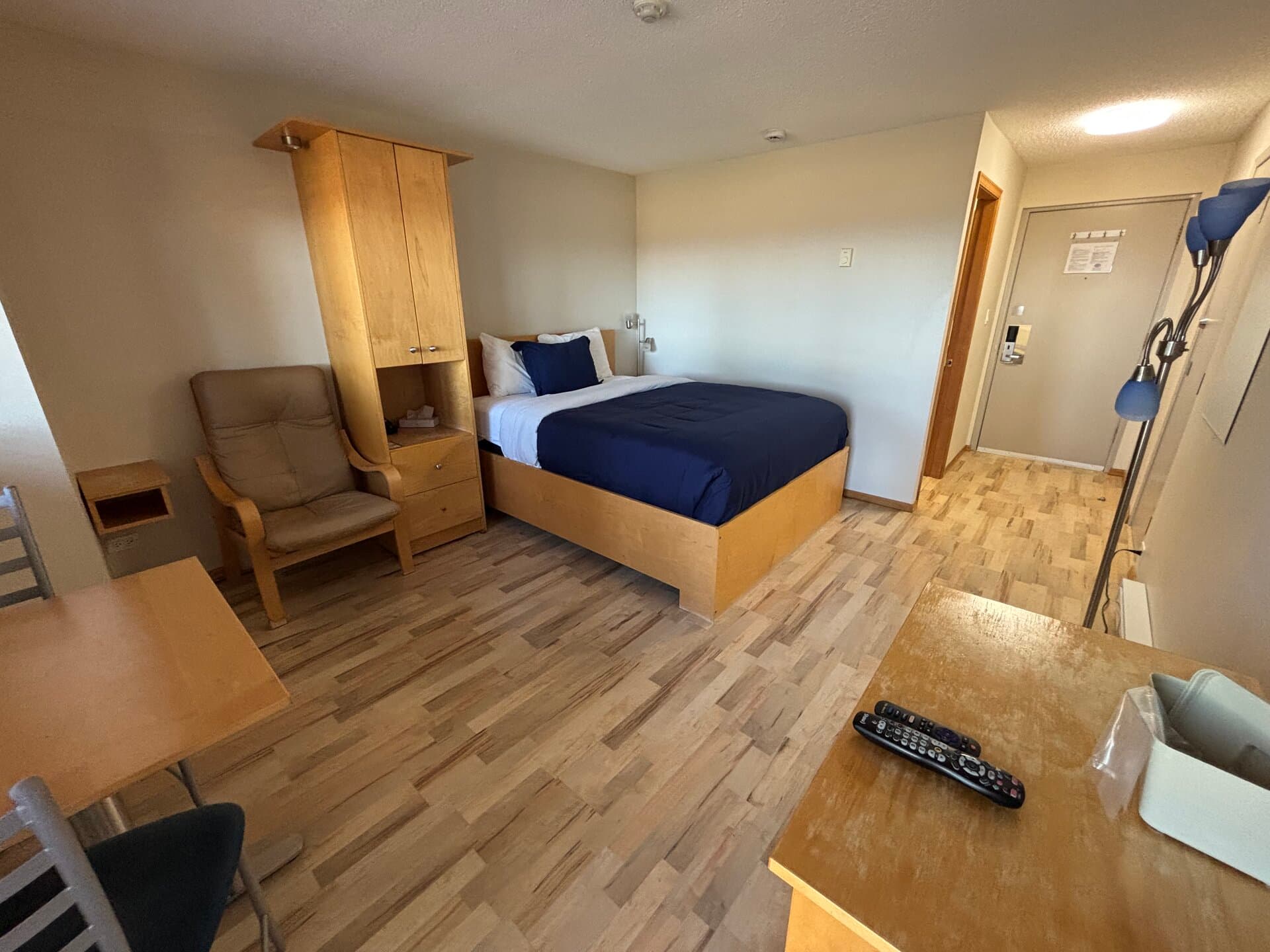 Queen bed with wardrobe, lounge chair, dining area, and television