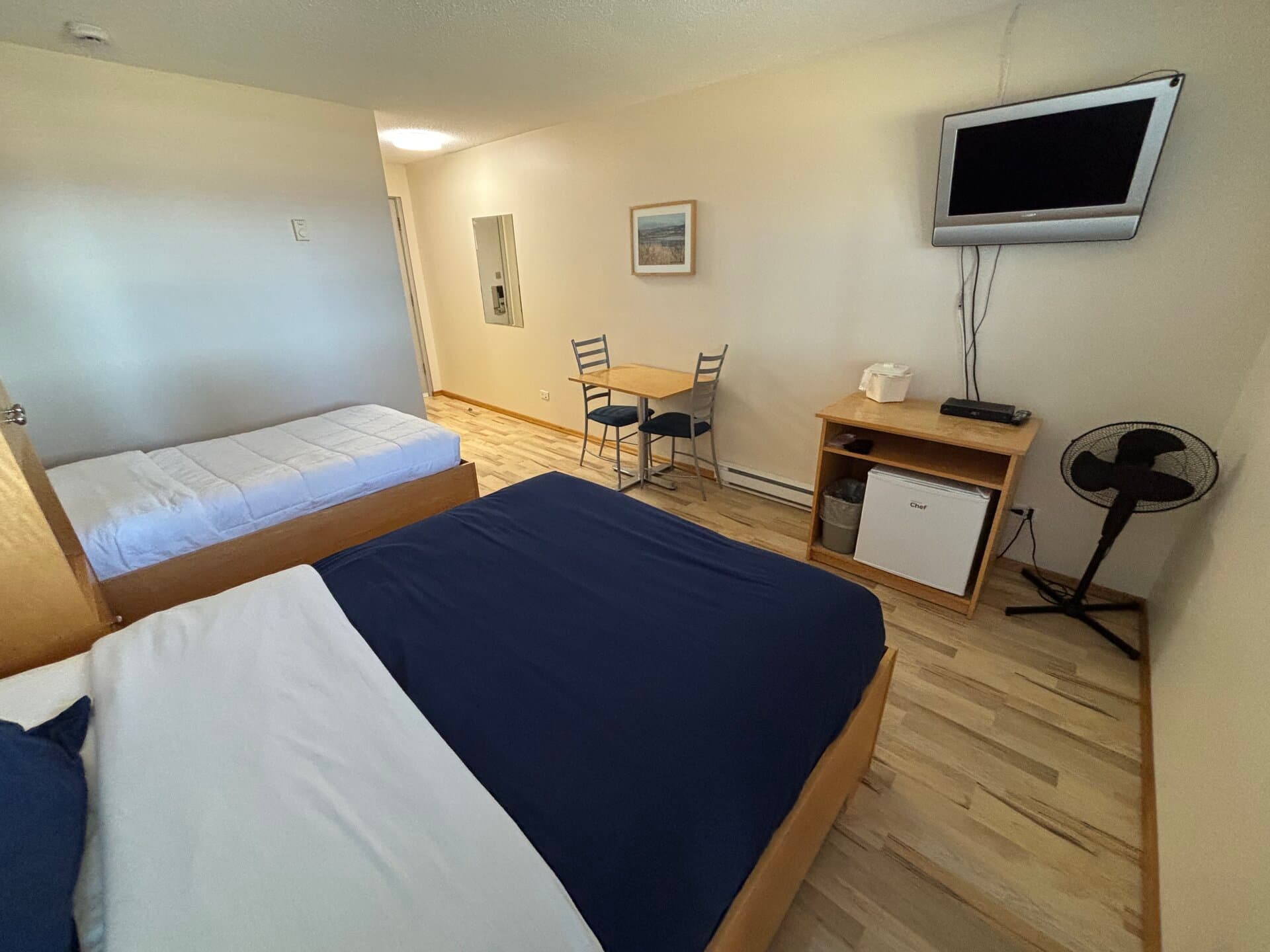 Double and twin beds with television, mini-fridge, fan, and dining area