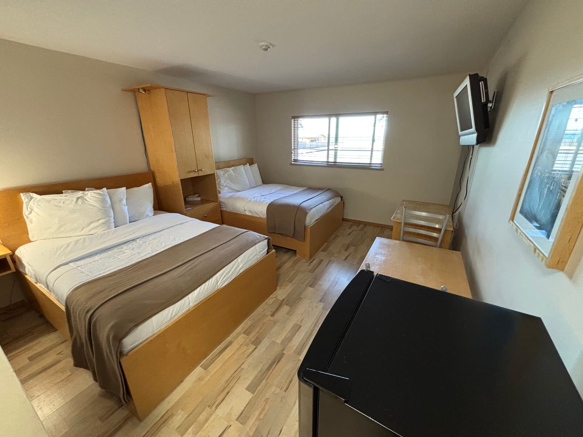 Two double beds with mini-fridge and walkway window views
