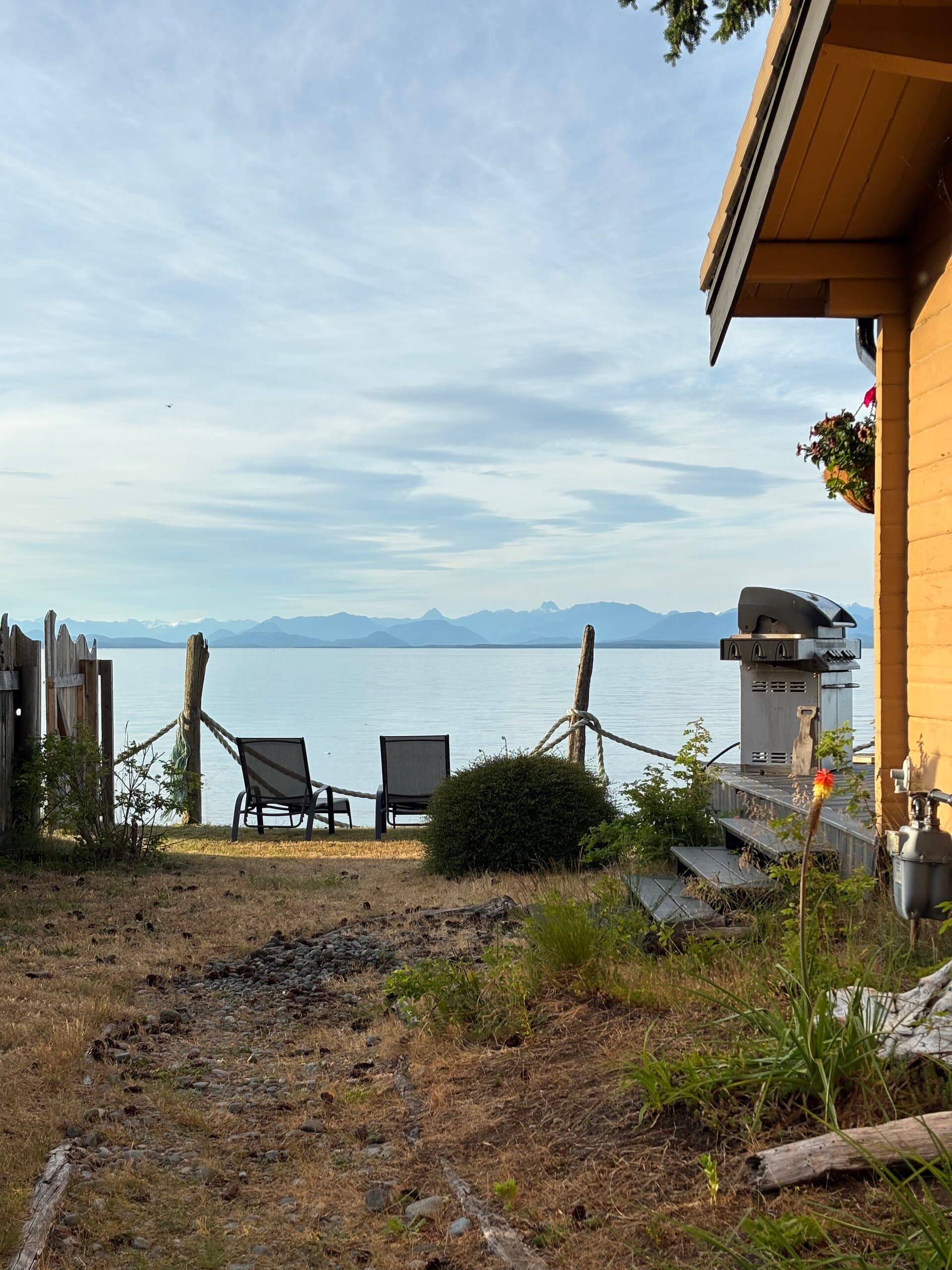 Backyard lounge chairs, BBQ, and rope fence with ocean and mountains