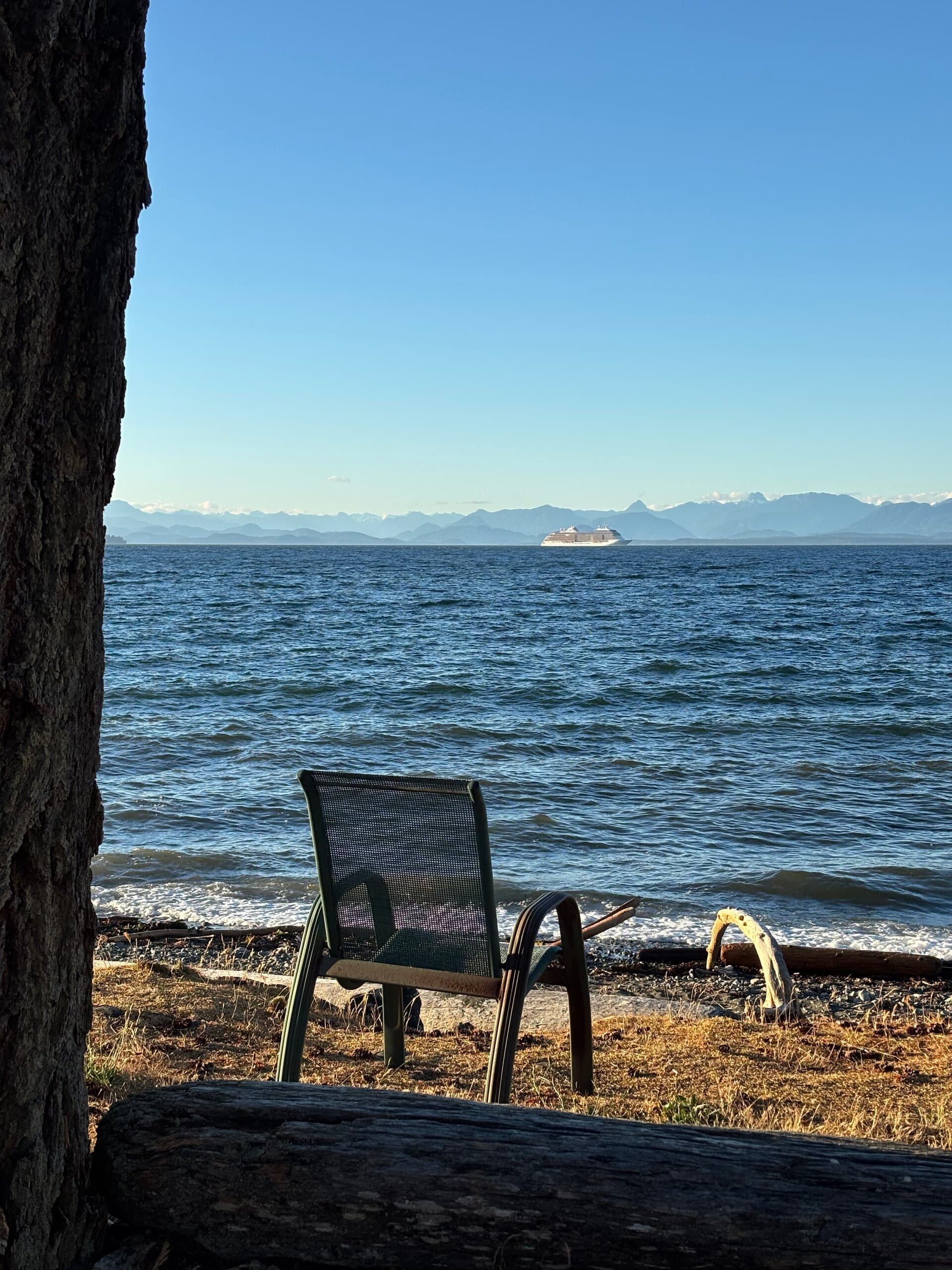 Beachfront chair with ocean, mountains, and passing ship